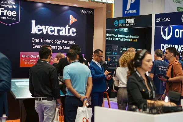 People attend a busy technology trade show, standing and talking near booths, including one for Leverate, which displays signage about brokerage solutions.