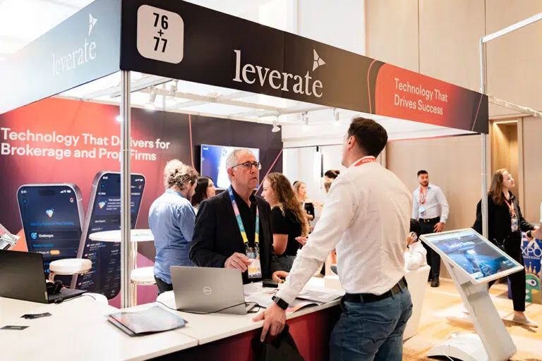 People interact at the Leverate booth during a business expo; promotional materials, screens, and banners display company technology offerings.